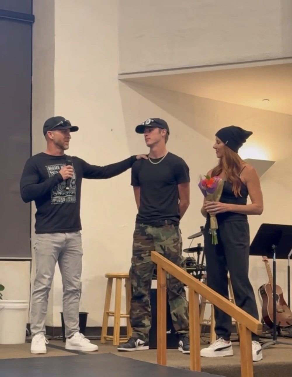 Kable holding a microphone with a hand on his son's shoulder at his son's homeschool graduation